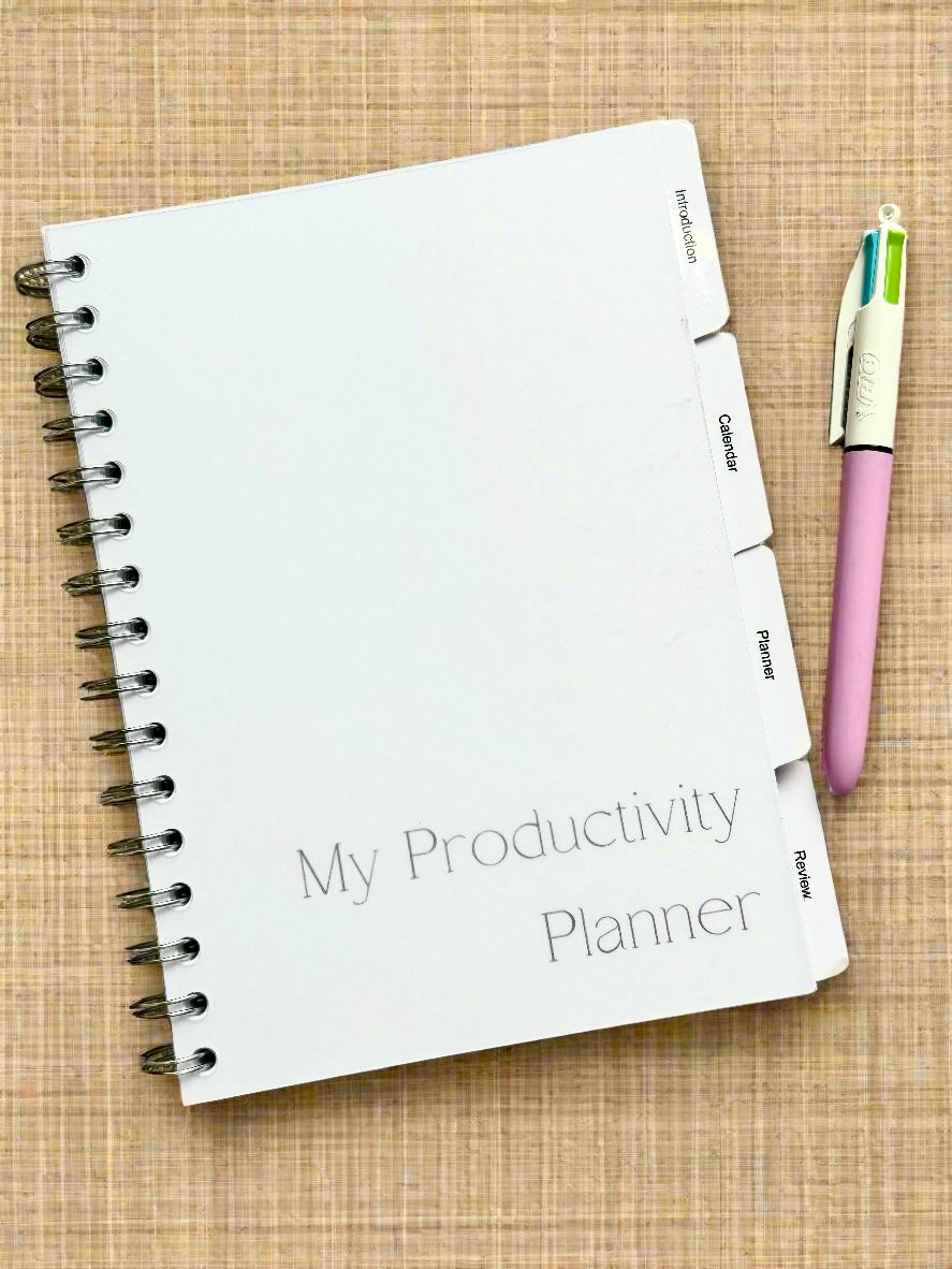 A white planner with a pink cover and a pink pen, labeled 'MY PRODUCTIVITY PLANNER'.