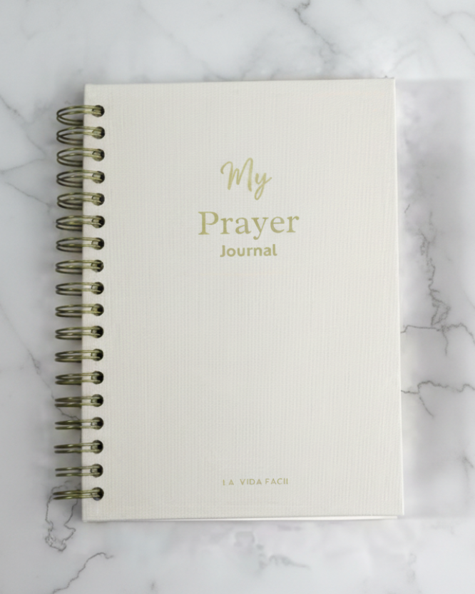 White prayer journal with gold text on a marble surface