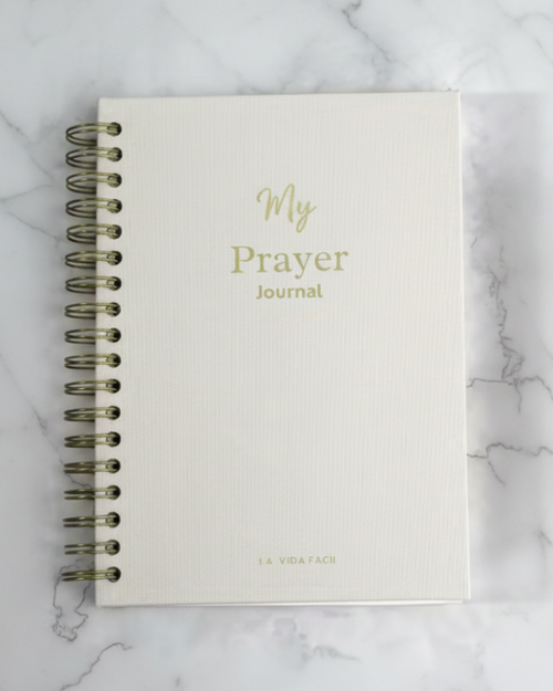 White prayer journal with gold text on a marble surface